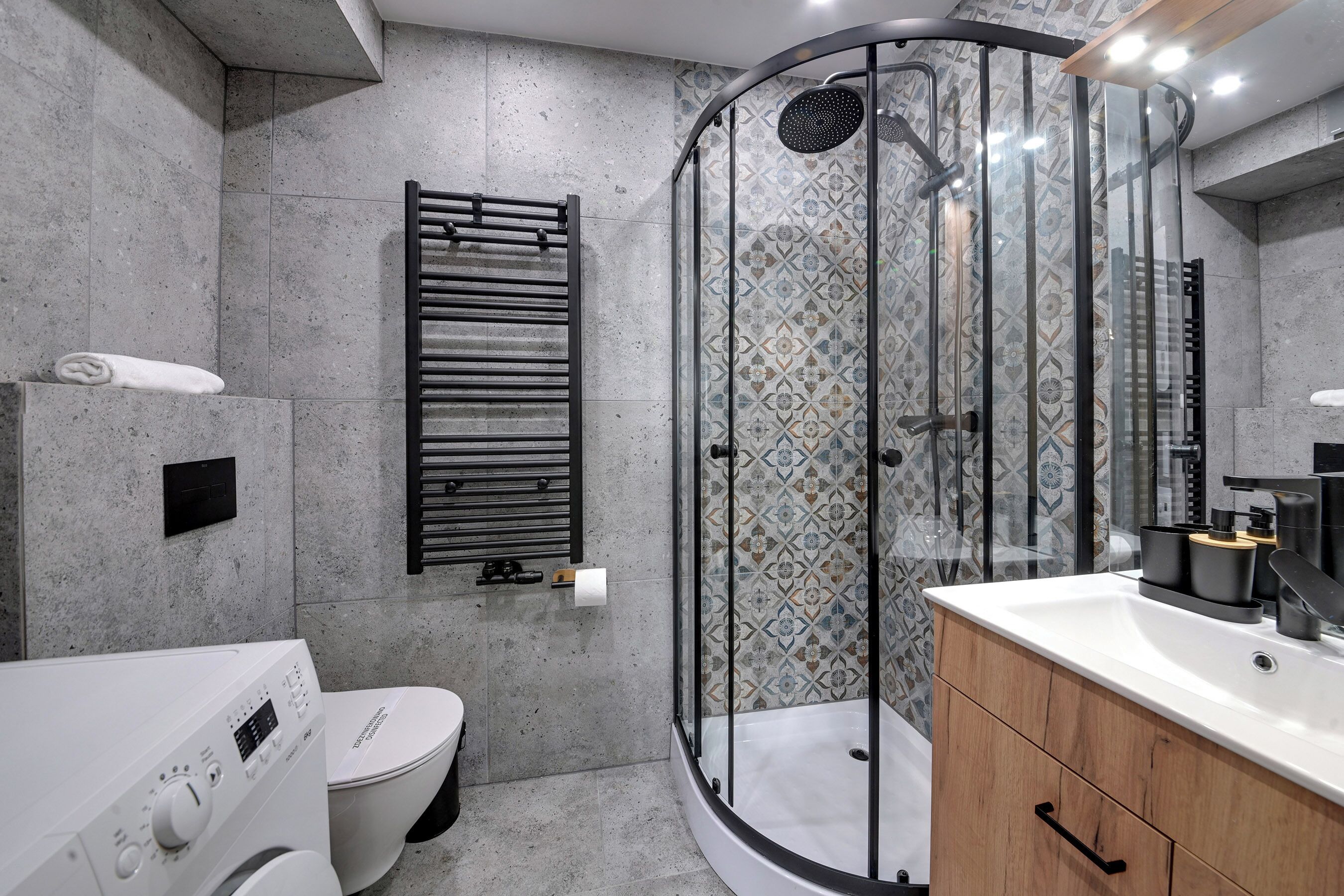 A modern bathroom with a glass-enclosed shower, a toilet, a washing machine, and a wooden vanity.
