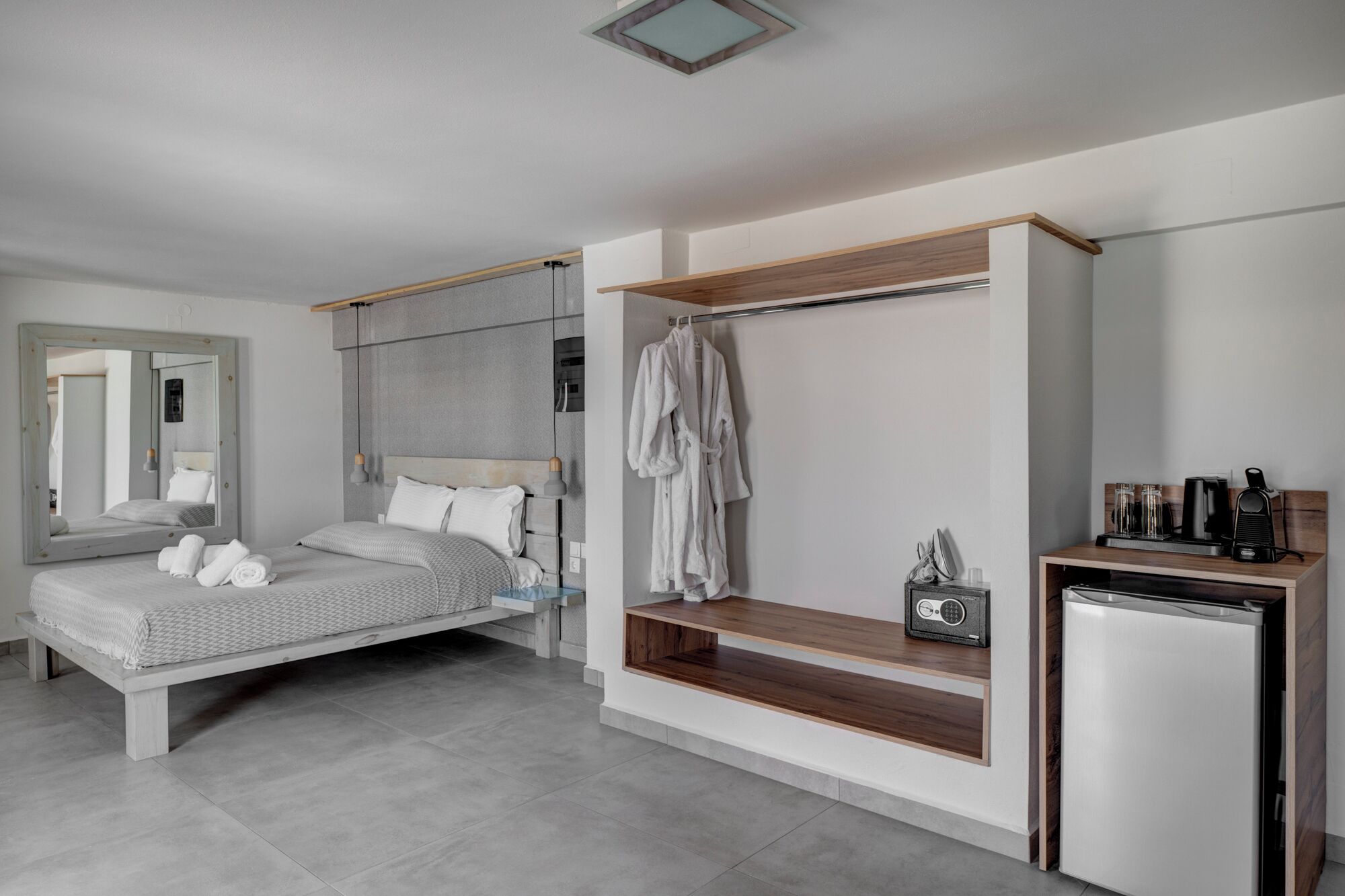 A modern bedroom with a bed, a built-in wardrobe, a small kitchenette, and a mirror.