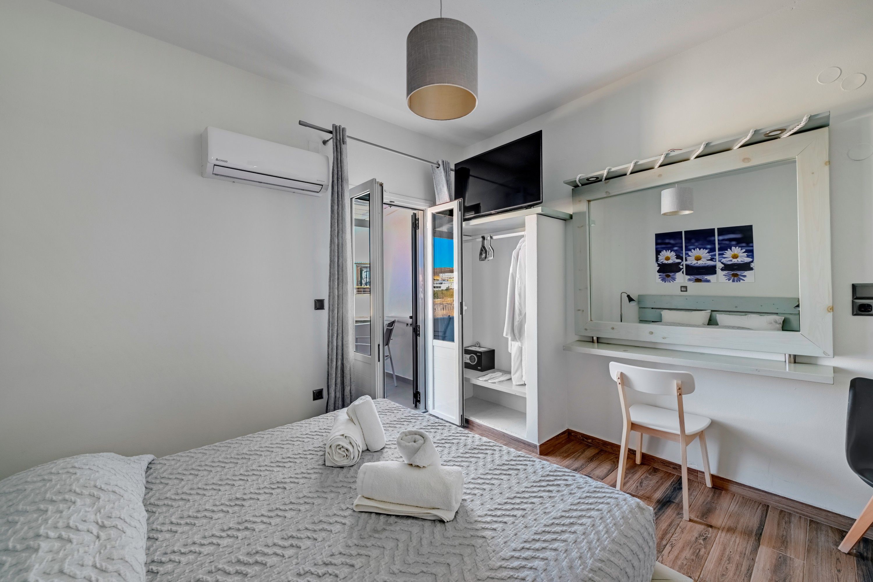 Un dormitorio moderno con cama, escritorio, silla, televisor y baño con ducha e inodoro.