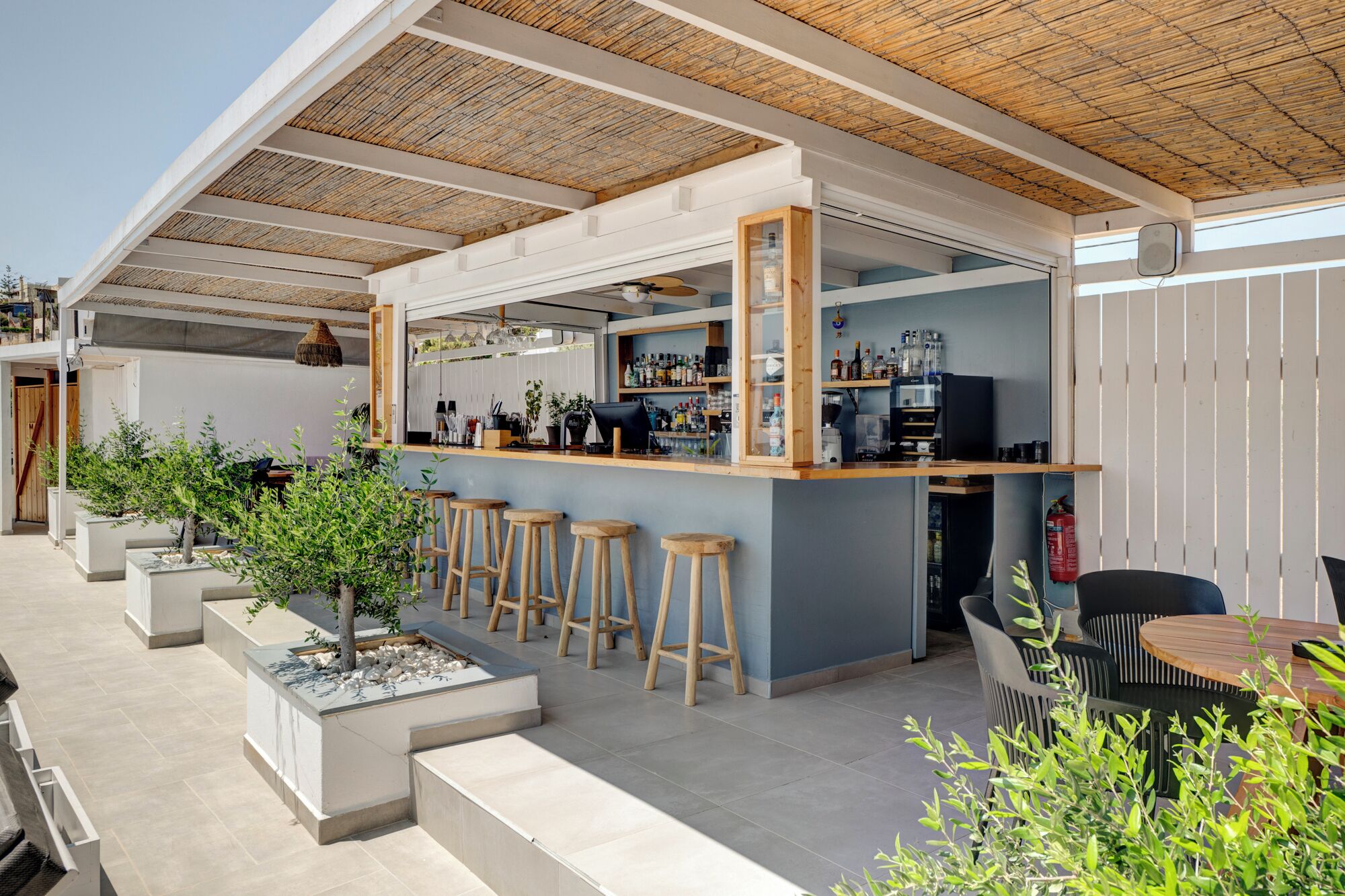 Zona de bar al aire libre con barra, taburetes y un espacio de estar con mesa y sillas.