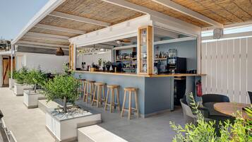 Zona de bar al aire libre con barra, taburetes y un espacio de estar con mesa y sillas.