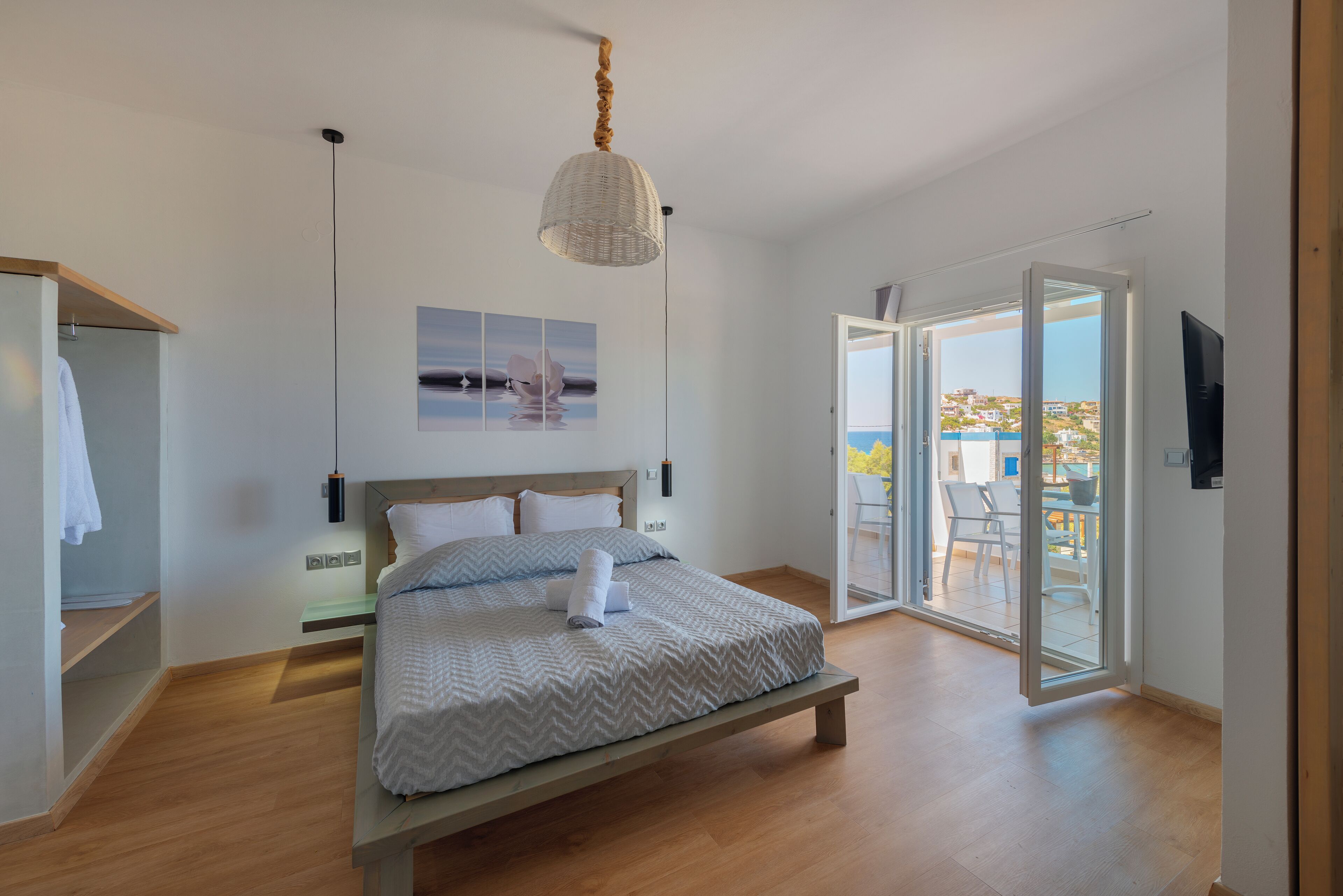Un dormitorio con cama, mesita de noche, lámpara colgante, vista al exterior y puerta que da a un balcón.