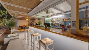 A modern bar area with white bar stools, a counter with a cash register, and shelves stocked with bottles. - Aegean Paradiso Vacation Club Adults Only (Syros)