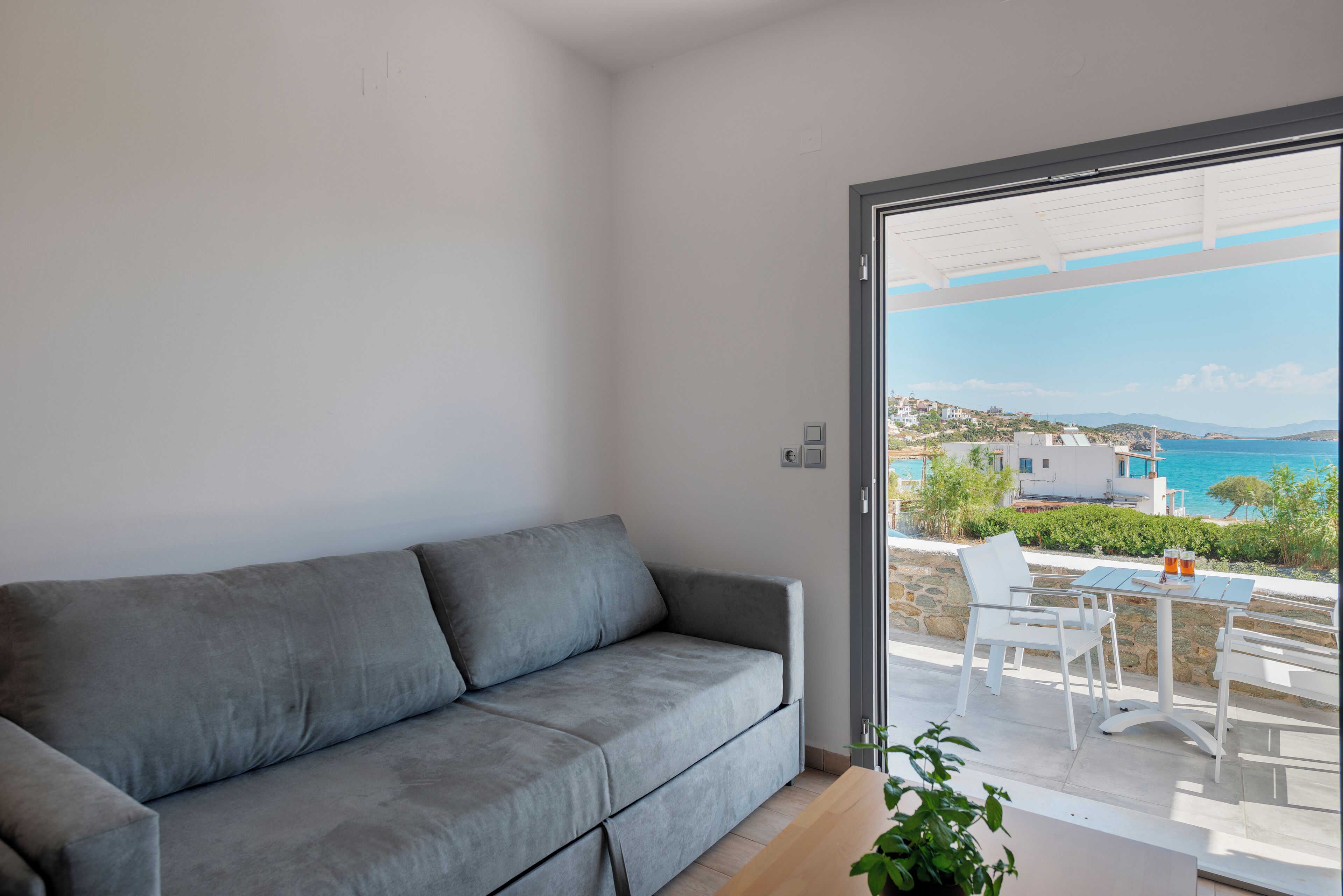 A modern living room with a grey sofa, a wooden coffee table, and a view of a coastal landscape through a glass door.