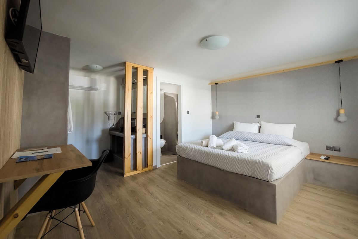 A modern bedroom with a bed, a desk, and a chair. There is a wooden partition separating the room.