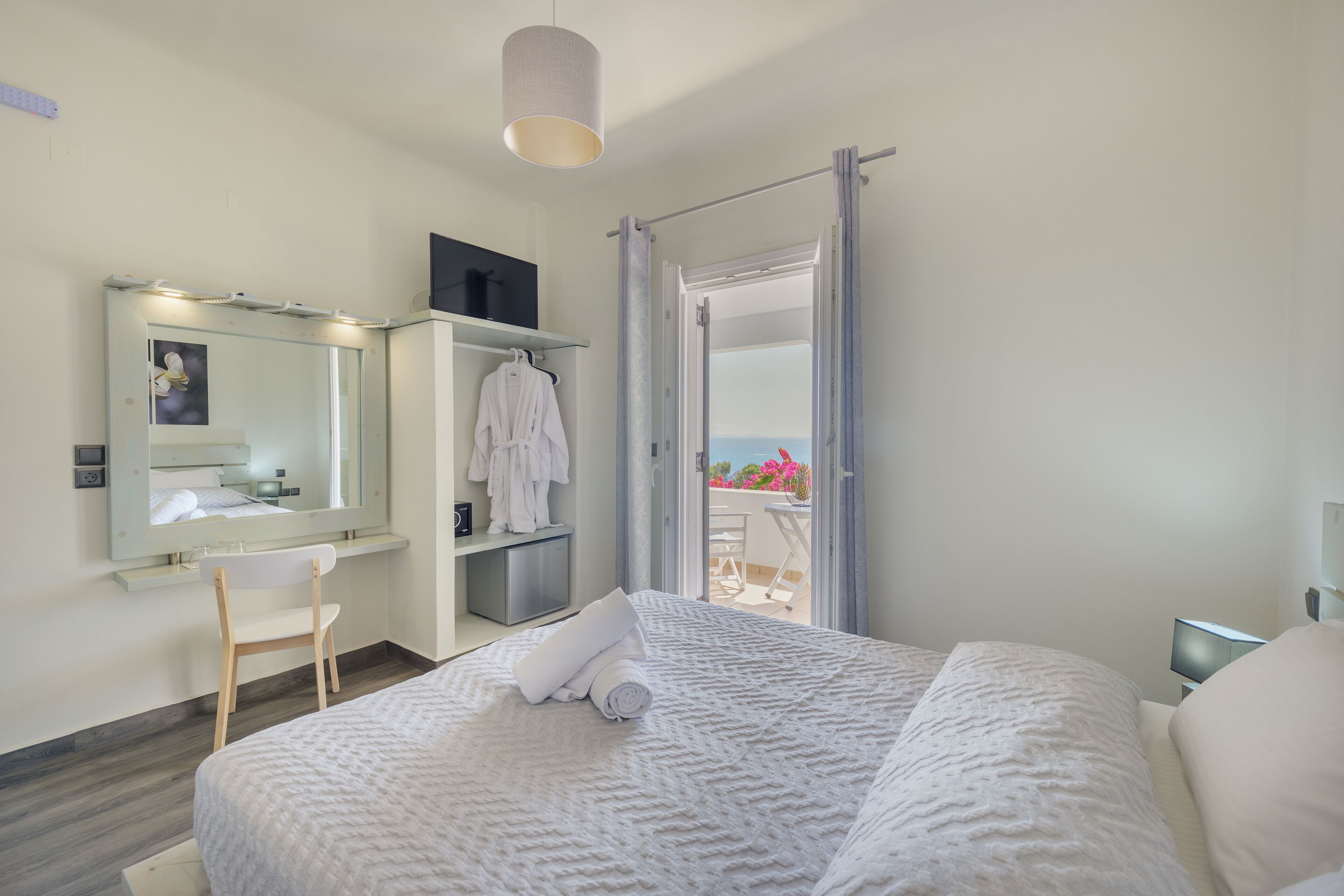 A modern bedroom with a large bed, a vanity with a mirror, a robe, and a view of the outdoors.