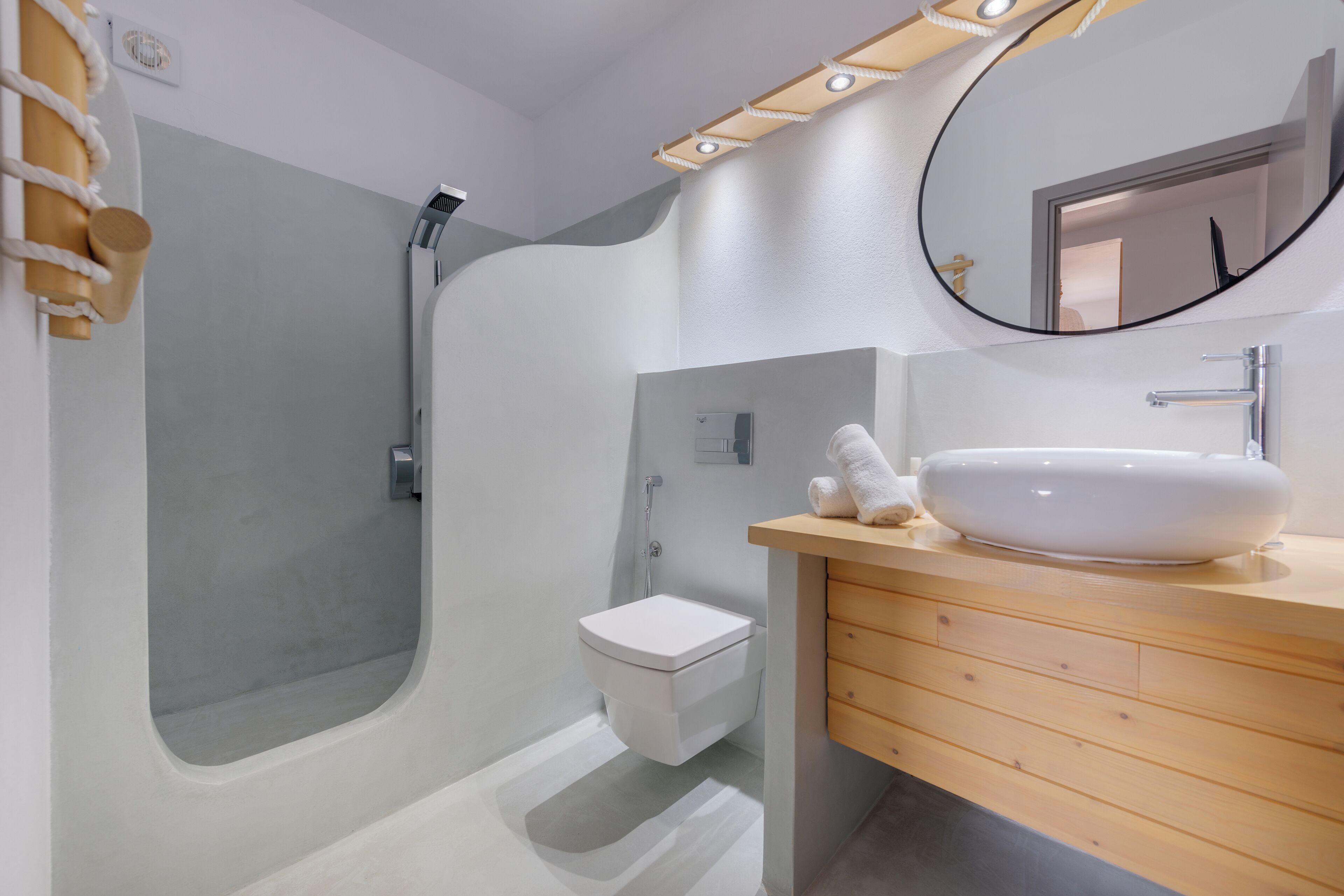 Un baño moderno con ducha integrada, inodoro blanco y tocador de madera con lavabo blanco.