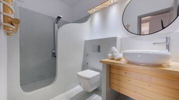 Un baño moderno con ducha integrada, inodoro blanco y tocador de madera con lavabo blanco.