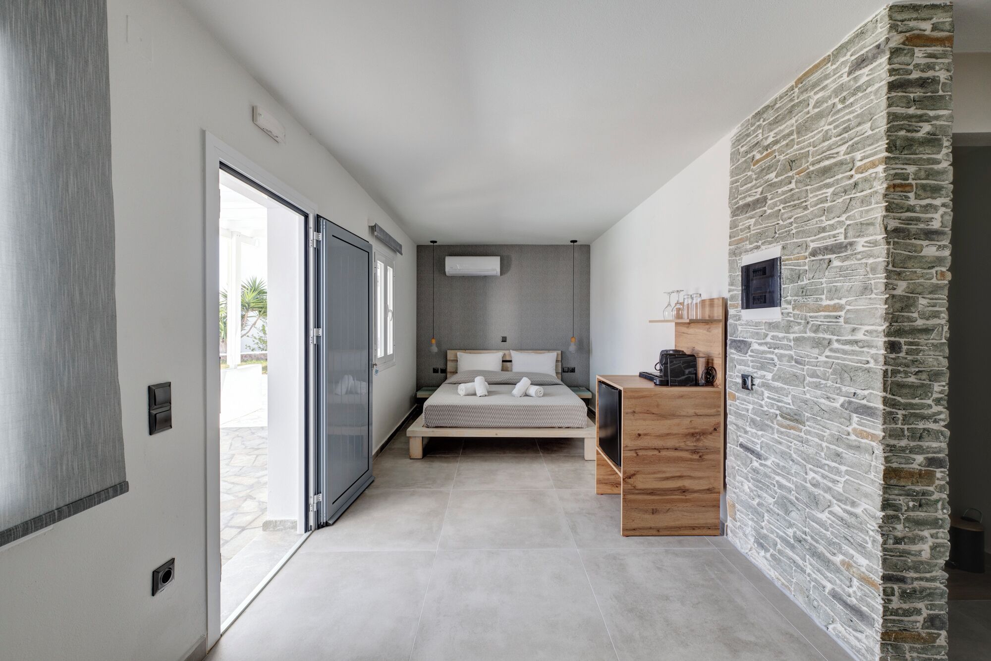 A modern bedroom with a large bed, a wooden nightstand, and a stone accent wall.