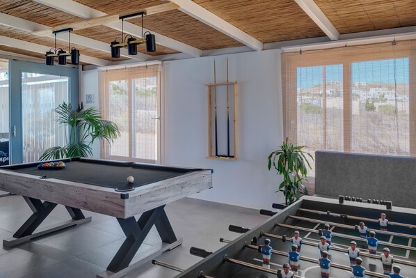 A room with a pool table, foosball table, and large windows with blinds. - Aegean Paradiso Vacation Club Adults Only (Syros)