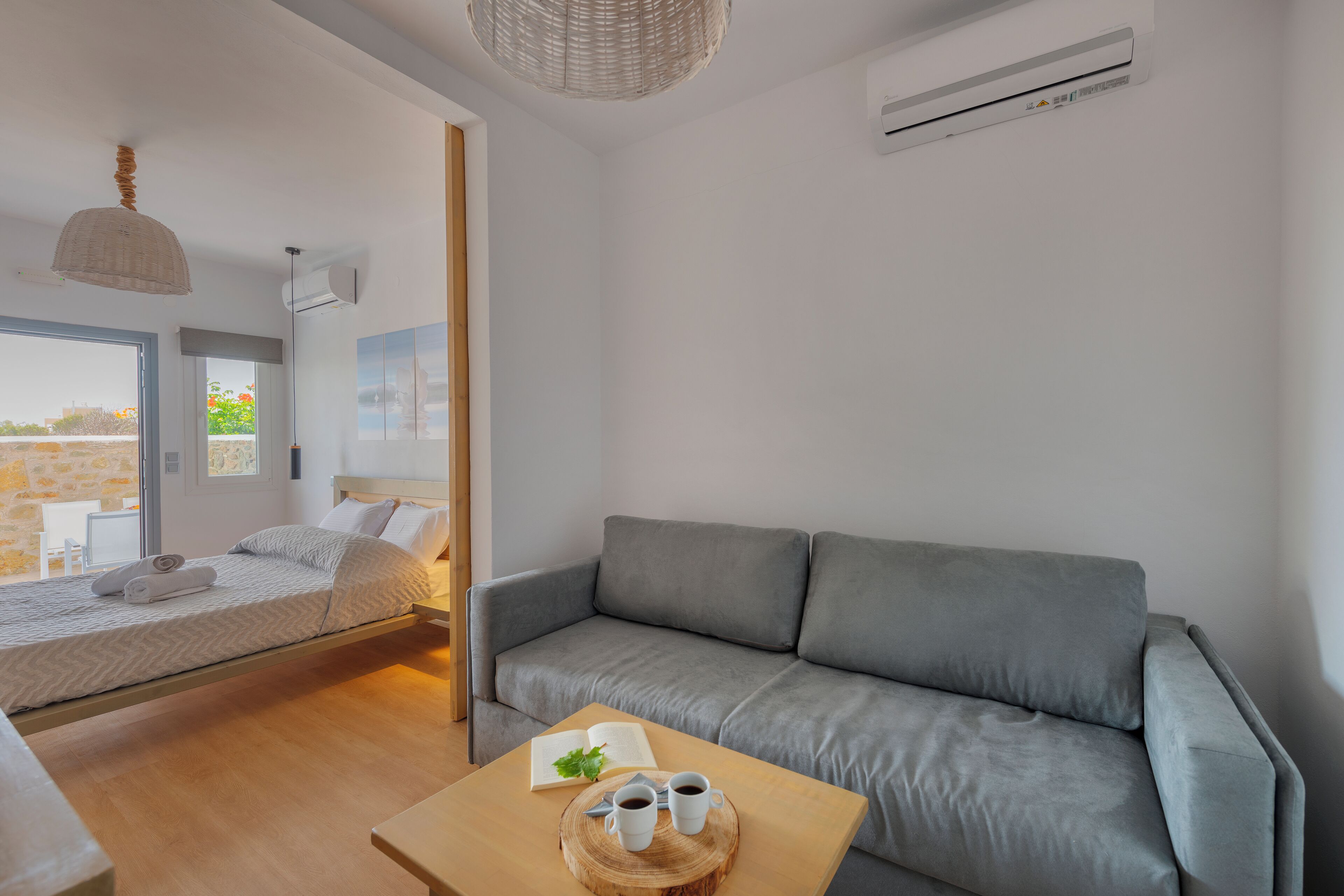 Une chambre à coucher moderne avec un lit, un canapé gris et une table en bois sur laquelle se trouvent un livre et des lunettes.