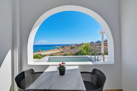 A room with a view of the sea, a pool, and a table with chairs.