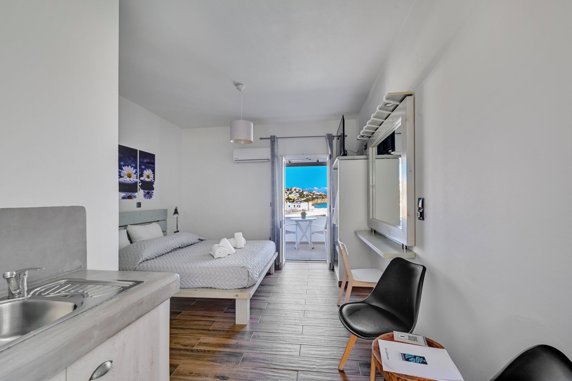 A compact hotel room with a bed, a small desk with a sink, a chair, and a TV.