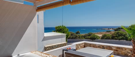 Un baño moderno al aire libre con una bañera, una mesita con un vaso de jugo de naranja y vista al mar.