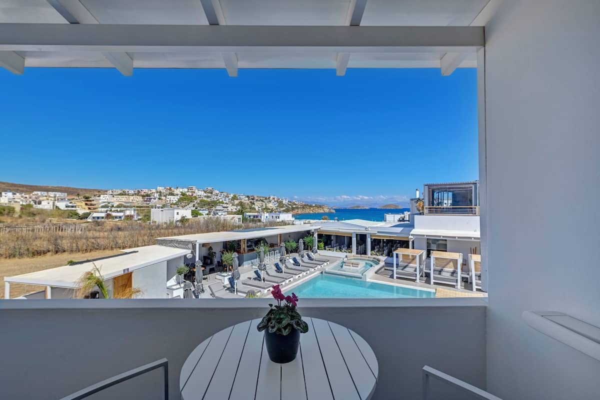 A balcony with a pool, lounge chairs, and a view of a coastal town.