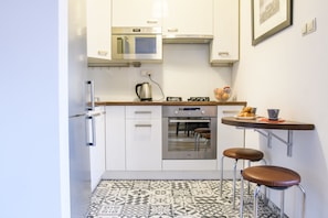 Compact kitchen with oven, coffee maker, and small table with two stools.