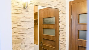 A wooden door with frosted glass panels, a stone-textured wall, and a light switch. - Chmielna Superior (Warsaw)