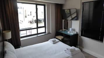 Habitación de hotel con una cama grande, un escritorio con silla, un televisor y una ventana con cortinas.