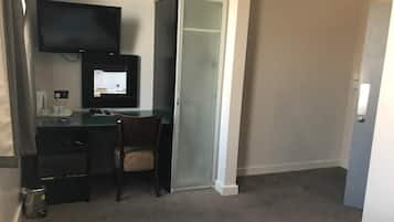 Een hotelkamer met een bureau, stoel, televisie en een kledingkast.