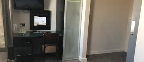 Quarto de hotel com escrivaninha, cadeira, televisão e guarda-roupa.