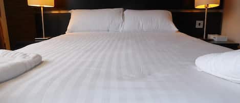 Una cama bien hecha con ropa blanca, dos lámparas de noche y un cabecero oscuro.