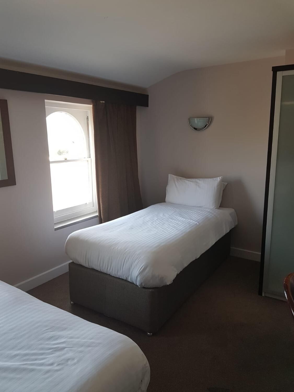 Ein Schlafzimmer mit einem Einzelbett, einem Fenster mit Vorhängen und einem kleinen Nachttisch.