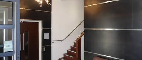 A modern lobby with a staircase, a brown leather sofa, and a chandelier.