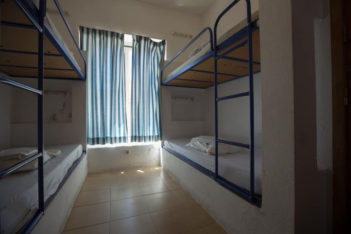 A dormitory room with bunk beds, a window with curtains, and a tiled floor.