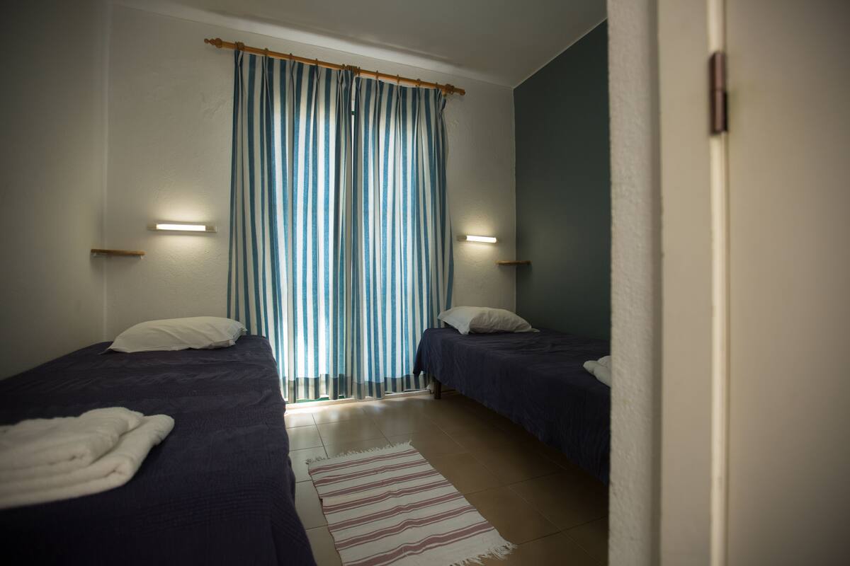 A bedroom with two beds, a striped rug, and a curtain.