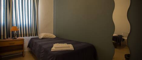 Une chambre à coucher avec un lit, une table de chevet, une lampe, un miroir et une fenêtre avec des rideaux.