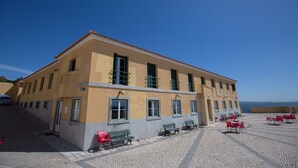 A building with a tiled patio, outdoor seating, and a view of the sea. - HI Oeiras - Pousada de Juventude - Hostel (Oeiras)