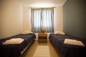 A twin room with two beds, a small table, and a window with curtains. - HI Oeiras - Pousada de Juventude - Hostel (Oeiras)