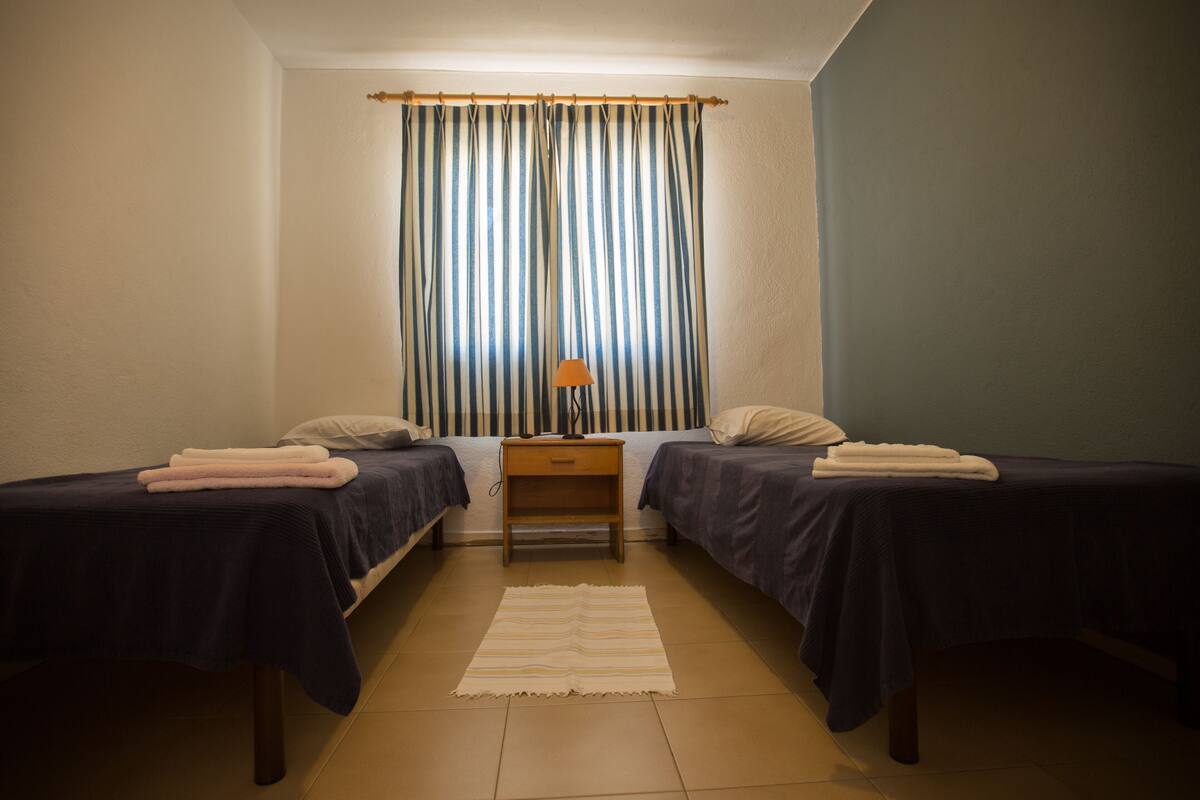 A room with two beds, a nightstand, a lamp, and a striped curtain.
