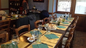 Un restaurante con una larga mesa de comedor dispuesta para una comida, sillas de madera y una zona de bar con botellas.