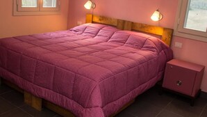 Una cama individual con cabecera de madera, pared rosa y mesita de noche con lámpara.