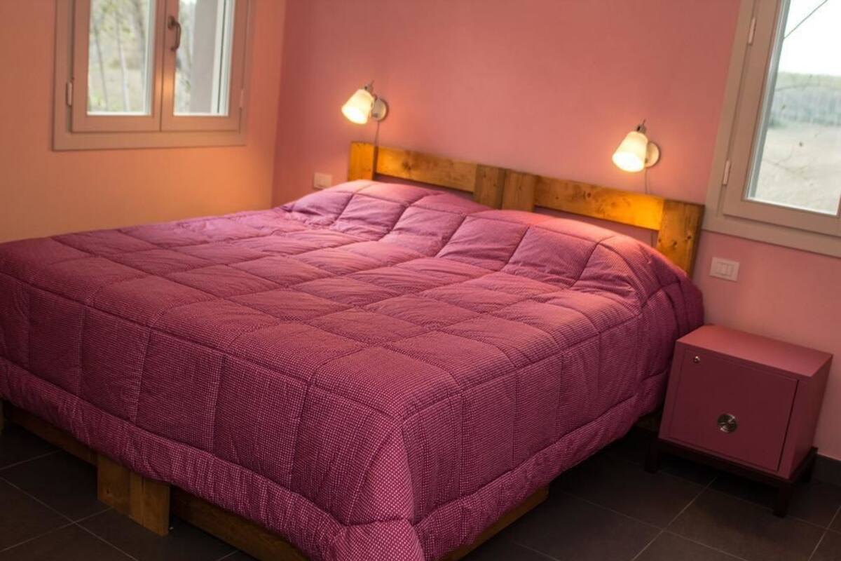 Ein Einzelbett mit Holz Kopfteil, eine rosafarbene Wand und ein Nachttisch mit Lampe.