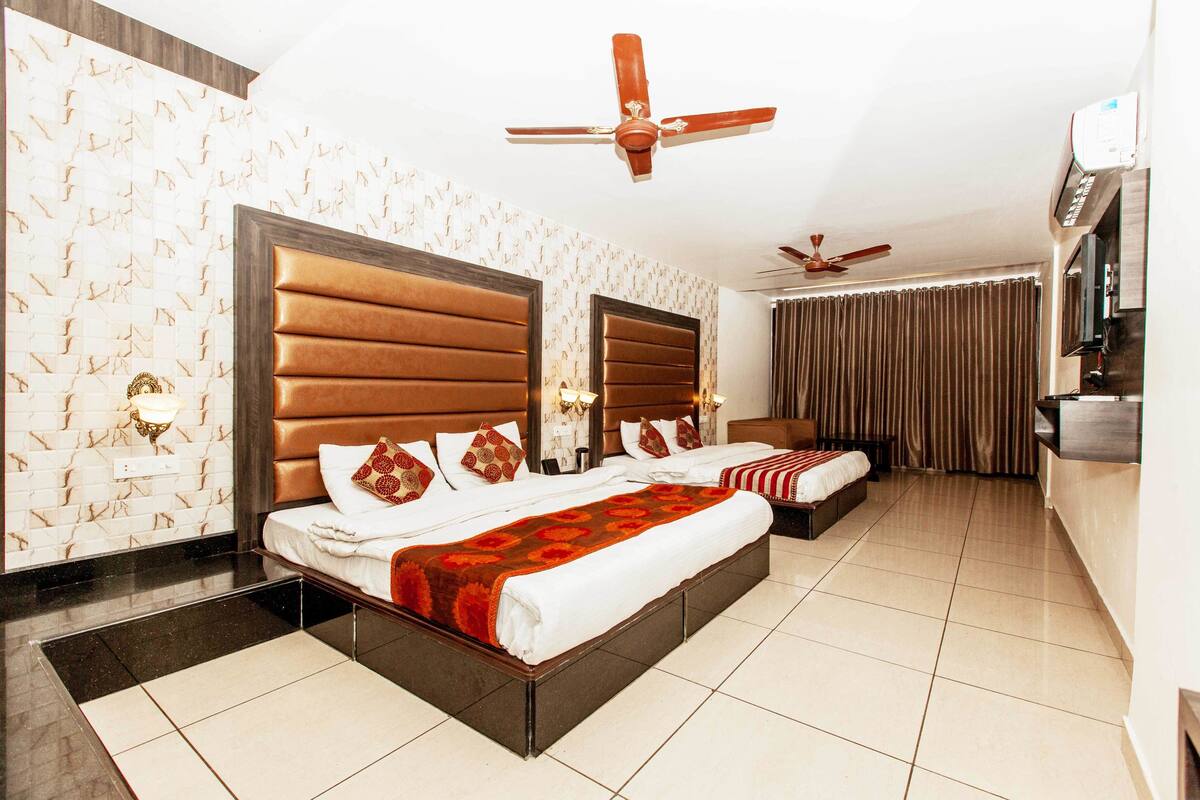 A hotel room with two beds, a ceiling fan, a minibar, and a bathroom with a shower curtain.