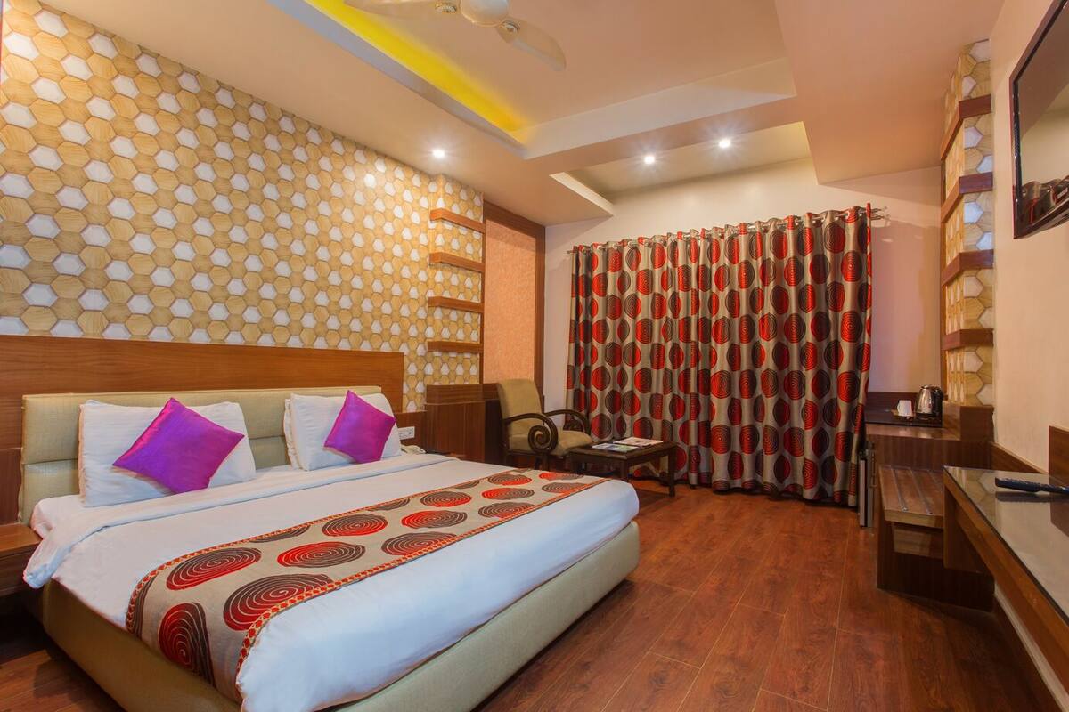 A hotel room with a large bed, a desk, a chair, and a window with curtains.