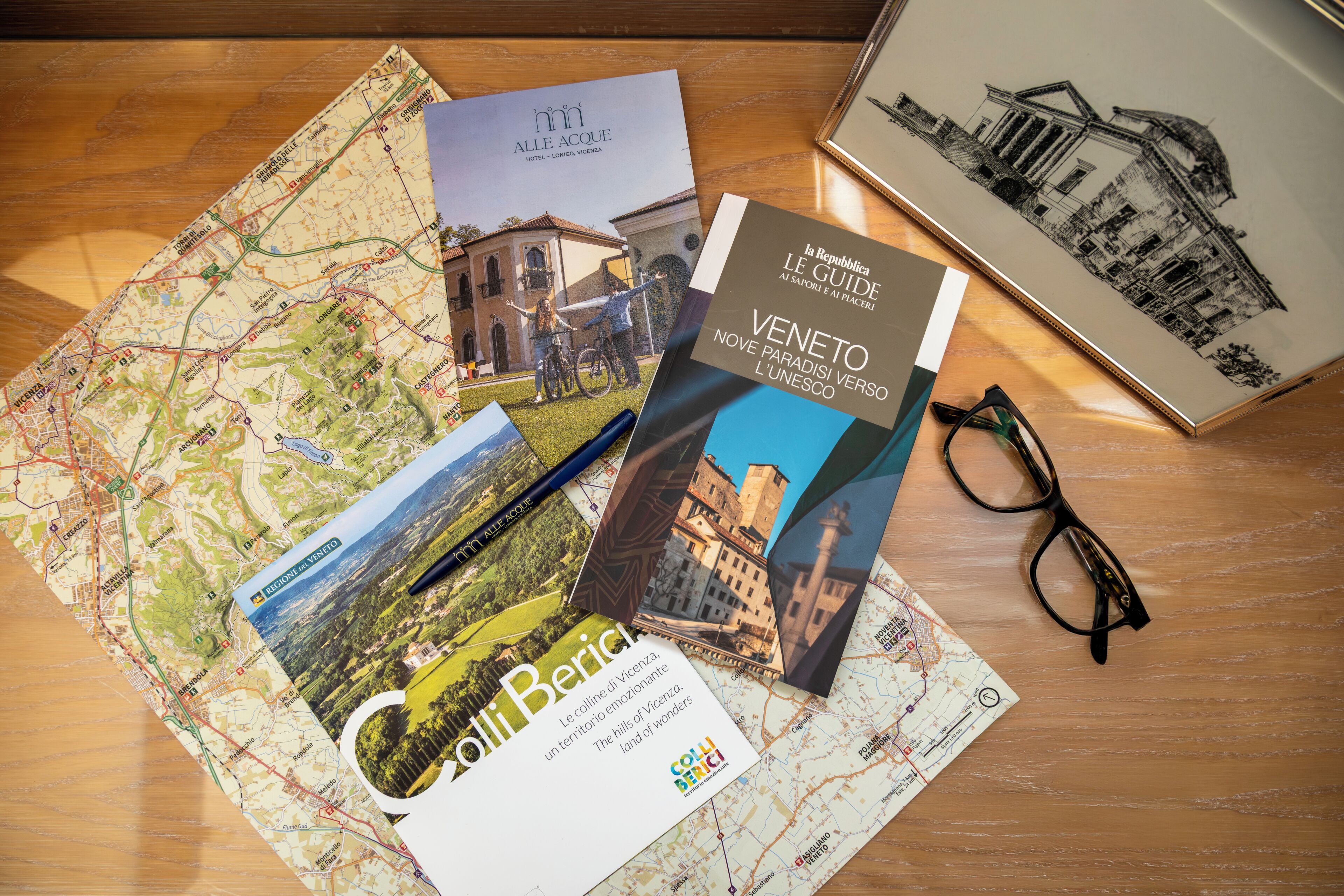 A map, a brochure, and a pair of glasses on a wooden surface.