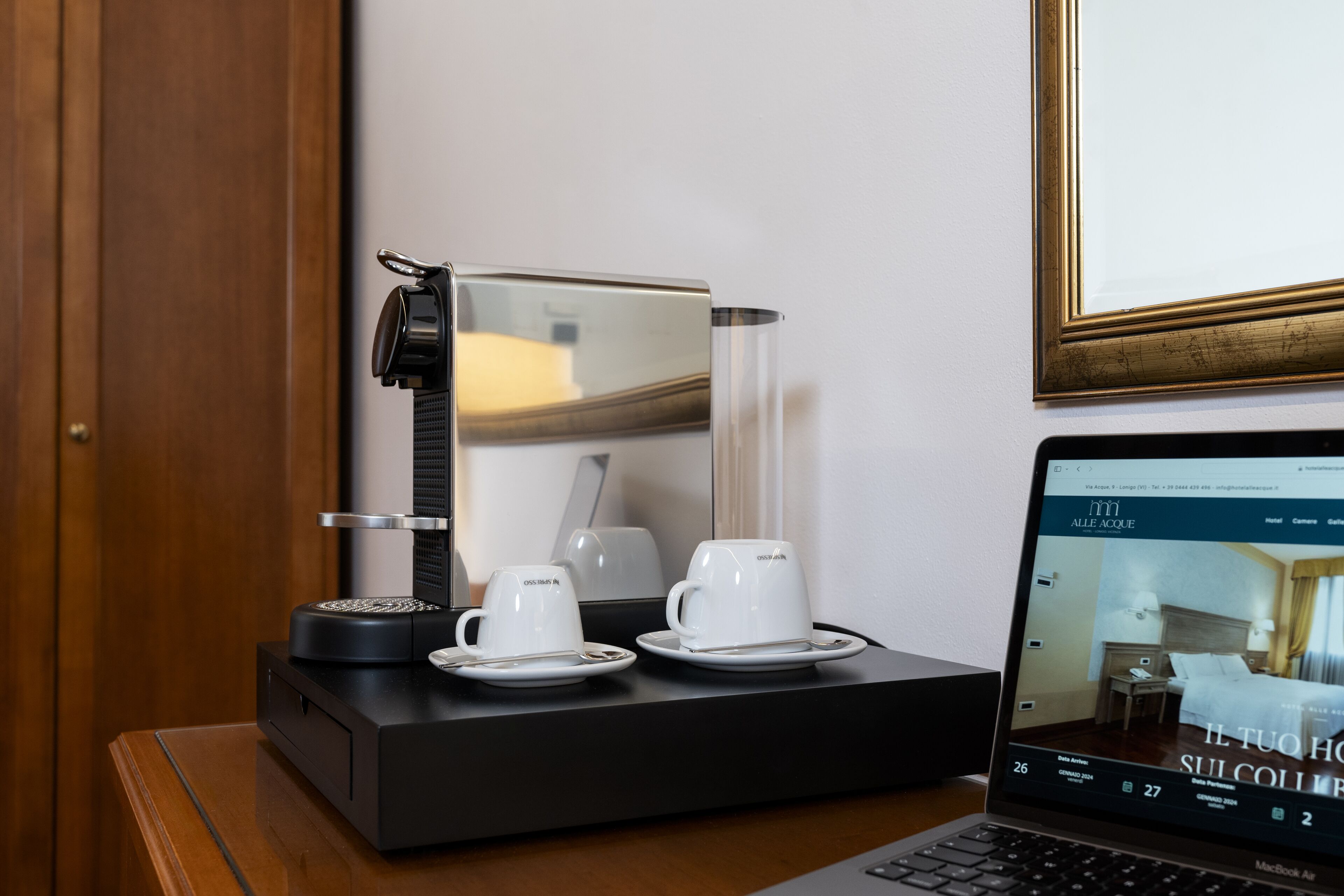 Habitación de hotel con cafetera, dos tazas y una computadora portátil mostrando la página web del hotel.
