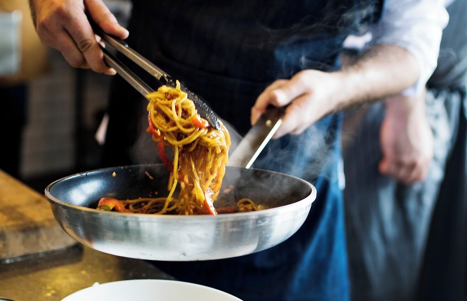 A person cooking spaghetti in a pan.