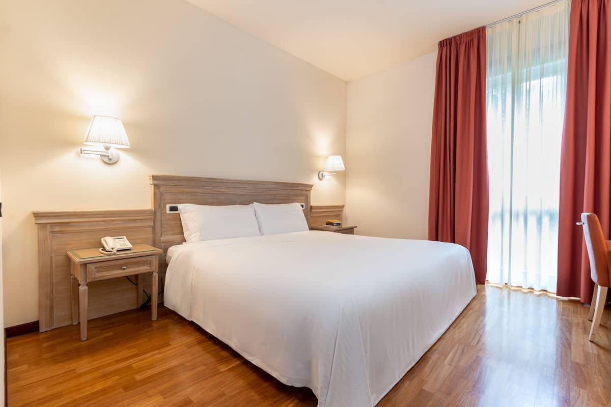 A hotel room with a large bed, two bedside tables with lamps, a telephone, and a chair.
