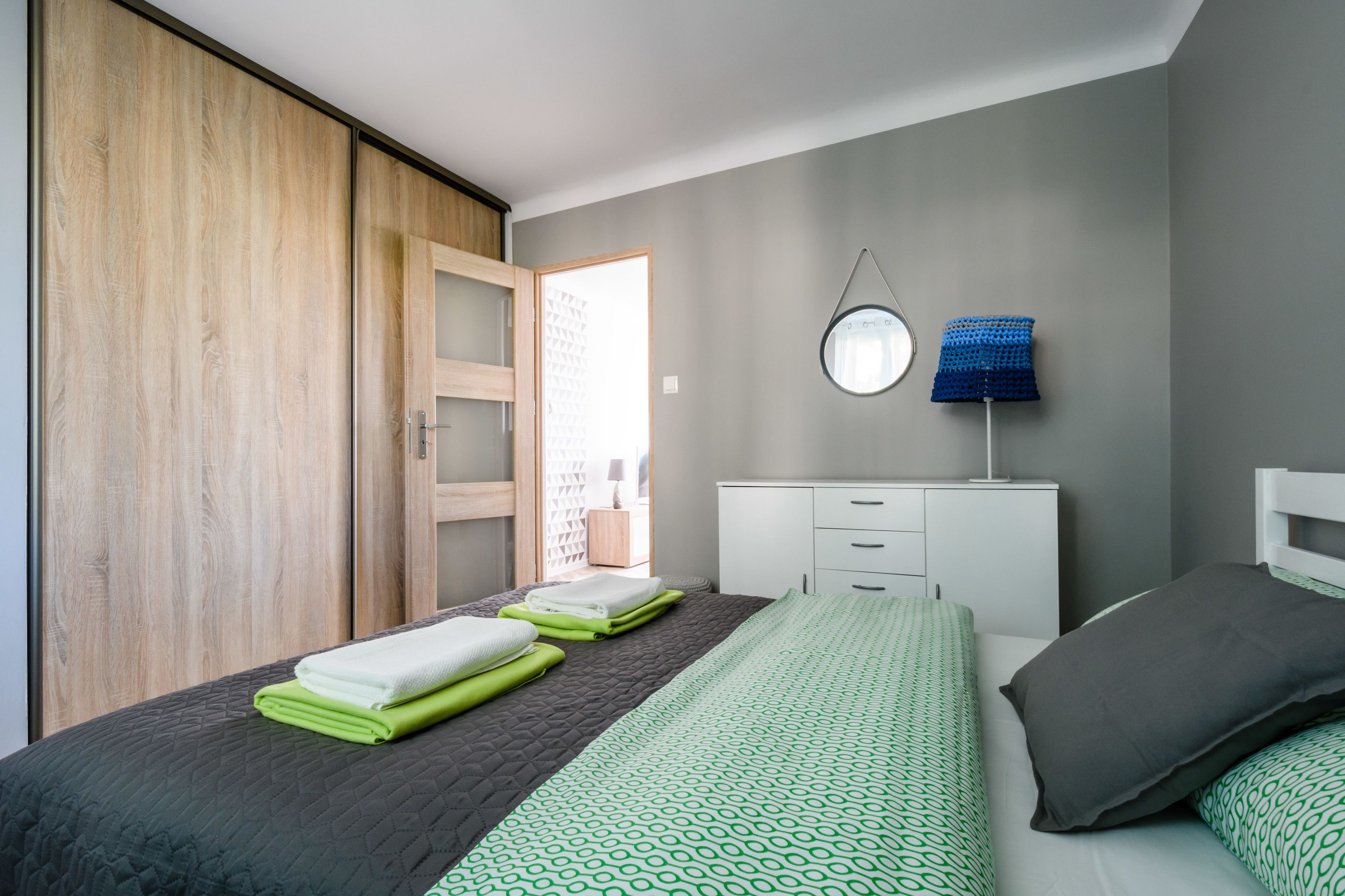 A bedroom with a bed, a wardrobe, a desk, and a lamp.