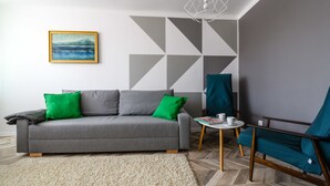 A modern living room with a grey sofa, green cushions, a small round table with a cup, and a teal armchair. - Chmielna Deluxe (Warsaw)