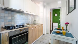 A modern kitchen with a gas stove, oven, and sink. There is a dining area with a table set for two, featuring a plate of food, a glass of juice, and a vase with flowers. - Chmielna Deluxe (Warsaw)