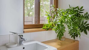 Une salle de bain avec un lavabo blanc, un miroir et une fenêtre donnant sur des arbres.