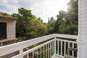 Un balcón con barandilla blanca, con vistas a un jardín con varios árboles y un muro de piedra.