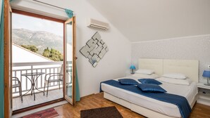 Un dormitorio con cama, mesita de noche, aire acondicionado instalado en la pared, balcón con mesa y sillas, y vistas a montañas.