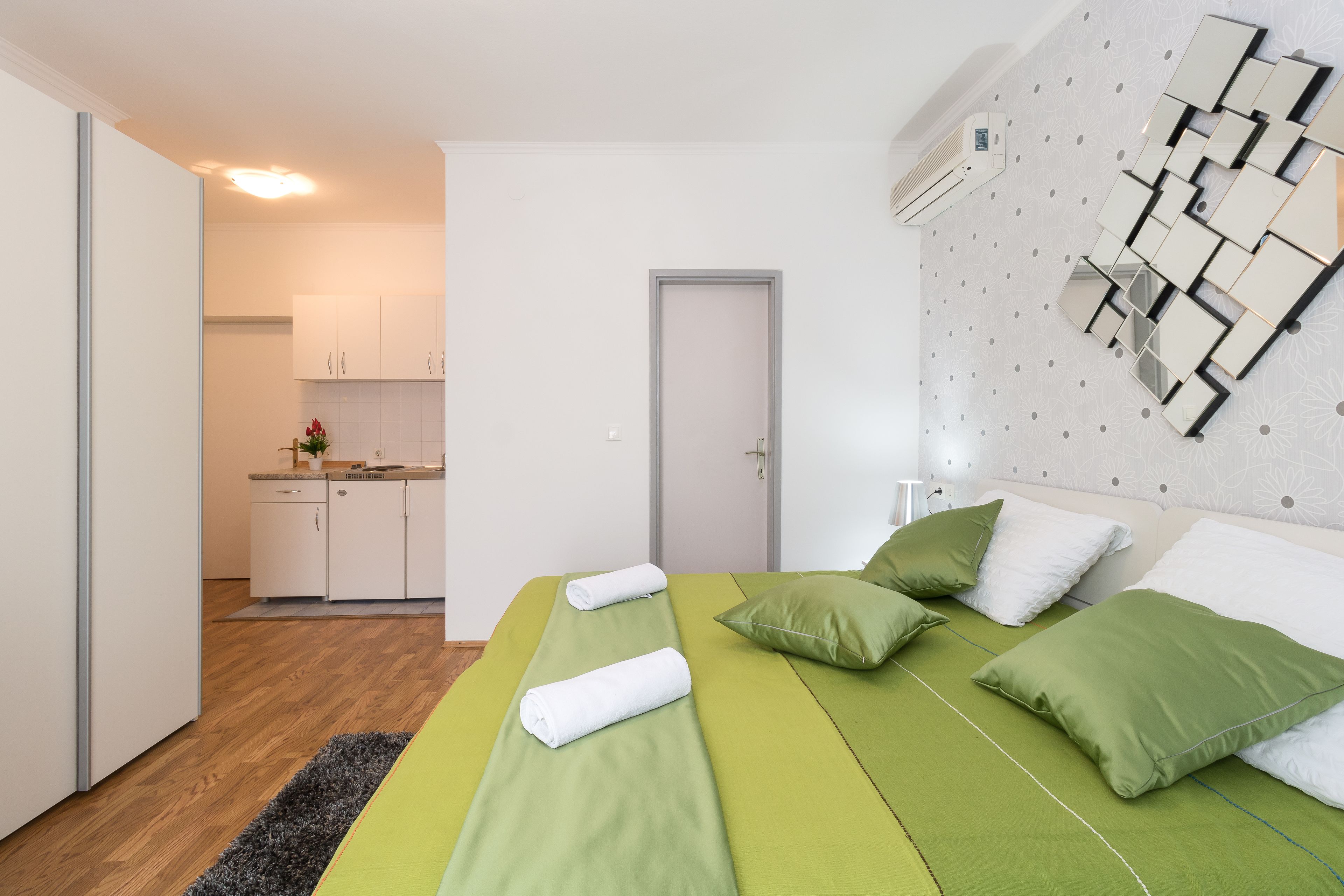 A modern hotel room with a green bed, white pillows, and a wall-mounted mirror.