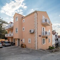 Un edificio de varios pisos con balcones, un letrero que dice "Villa Vini" y coches estacionados al frente.